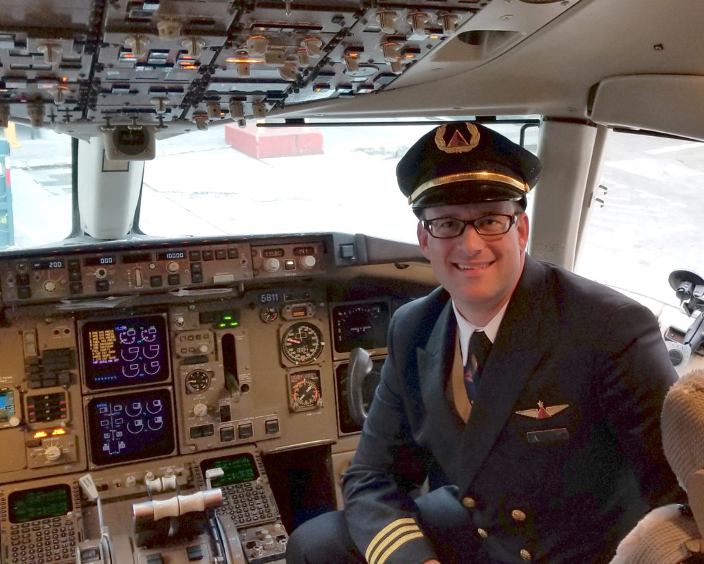 An airline pilot smiling in the cockpit of a commercial airline jet.