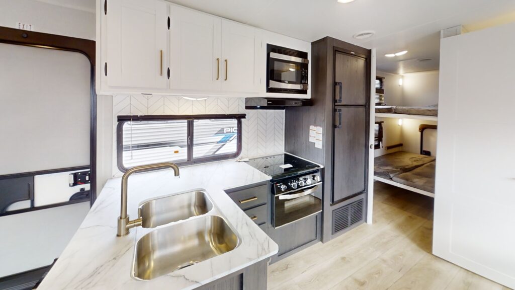 Kitchen in the Pioneer BH281 travel trailer, featuring stainless steel appliances, a spacious countertop, and stylish wooden cabinets with ample storage.