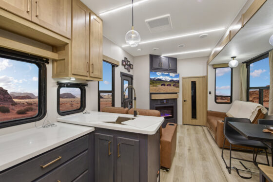 Interior of the 2025 Heartland Cyclone 4215 featuring a modern kitchen with stainless steel appliances, dark wood cabinetry, and a spacious living area with plush seating.