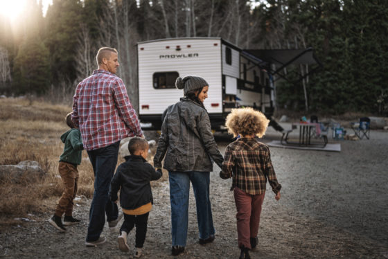 A family with three young kids walking toward a Heartland RV.