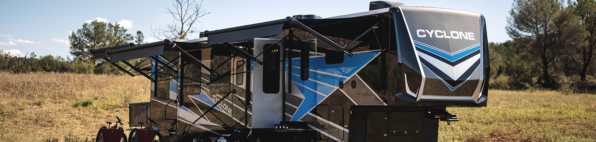 A lifestyle image featuring the Cyclone 2023 toy hauler parked in a scenic camping site surrounded by trees.