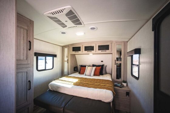 Interior view of the cozy bedroom in a Sundance Ultra Lite travel trailer, featuring a comfortable bed, overhead storage, and windows for natural light.