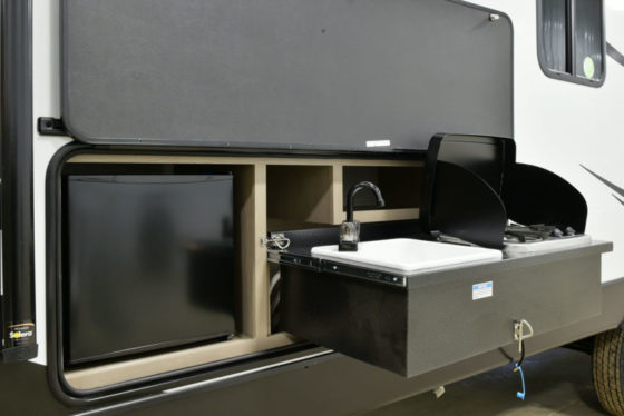 Outdoor kitchen of a Sundance Ultra Lite travel trailer, featuring a grill, sink, and ample counter space.