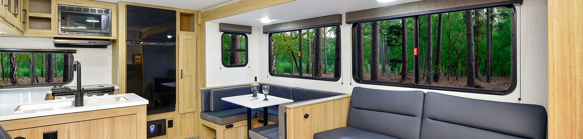The image showcases a Heartland Prowler travel trailer parked in an open area with a scenic background of trees and a clear sky. The RV features a sleek, aerodynamic design with a bold black, white, and blue exterior. The Prowler branding is prominently displayed on the front, along with stylish graphics along the side. The trailer is equipped with multiple windows for natural light, a sturdy entry door with fold-out steps, and stabilizing jacks for a secure setup. The front end includes a hitch and propane tanks, ready for towing and adventure. This travel trailer is designed for comfort, durability, and outdoor exploration.