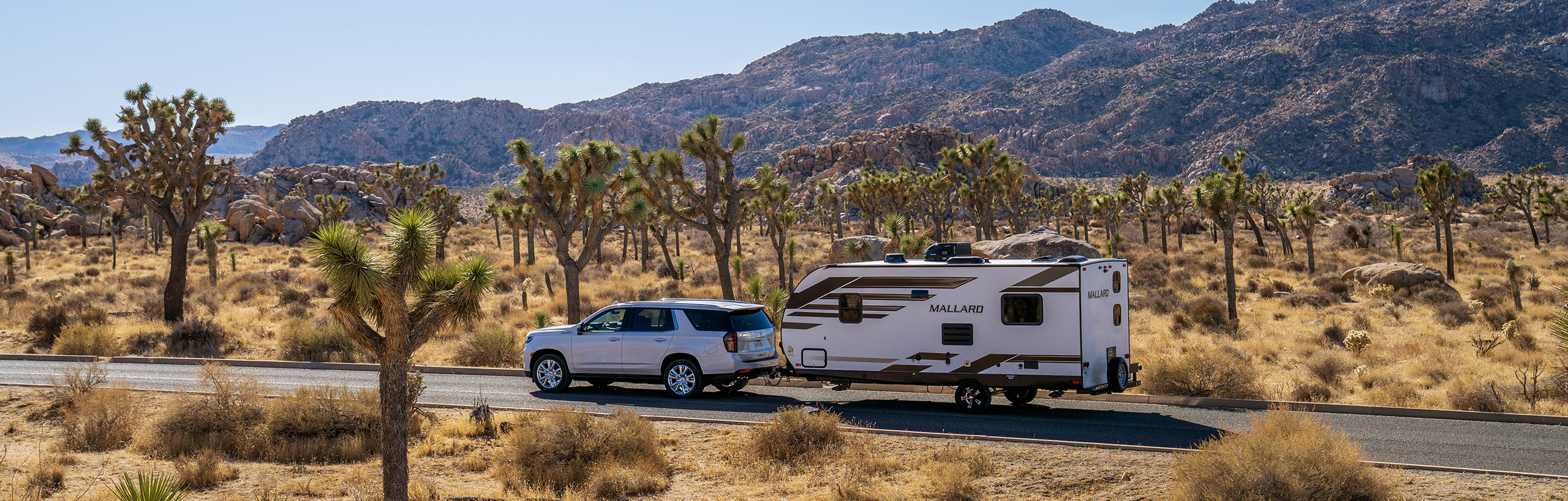 A lineup of sleek and lightweight Heartland Ultralite travel trailers against a blue sky backdrop.