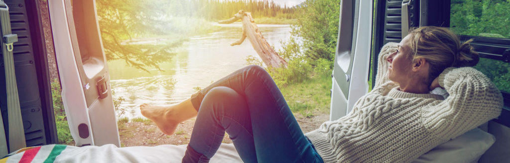 A woman reclining on an RV bed, looking out at a beautiful view while enjoying the healthy lifestyle habit of relaxation