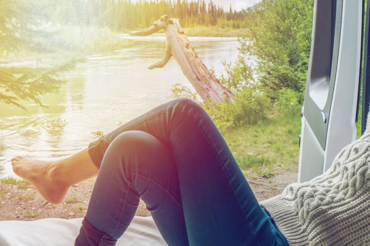 A woman reclining on an RV bed, looking out at a beautiful view while enjoying the healthy lifestyle habit of relaxation