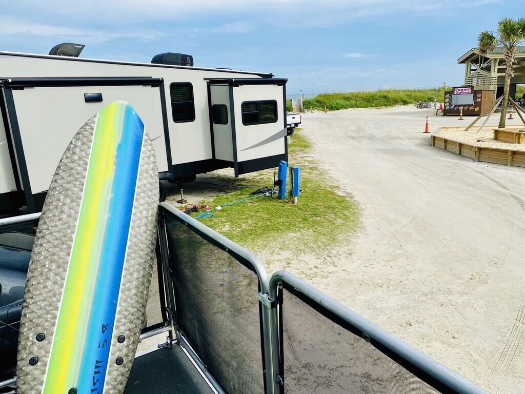 A surf board leaning against an RV toy hauler patio rail at an RV campsite.