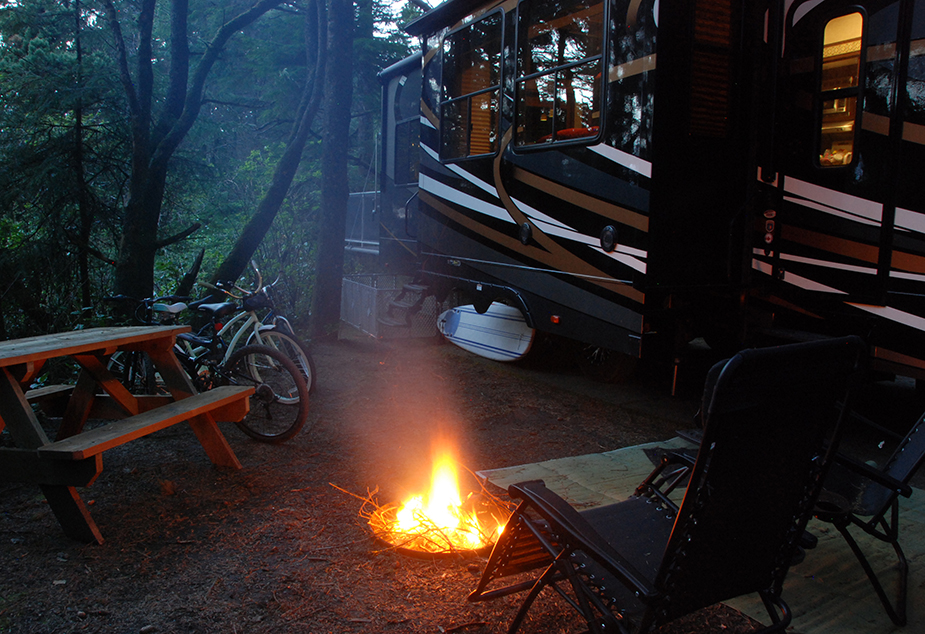 A campfire burning at an RV campsite at dusk