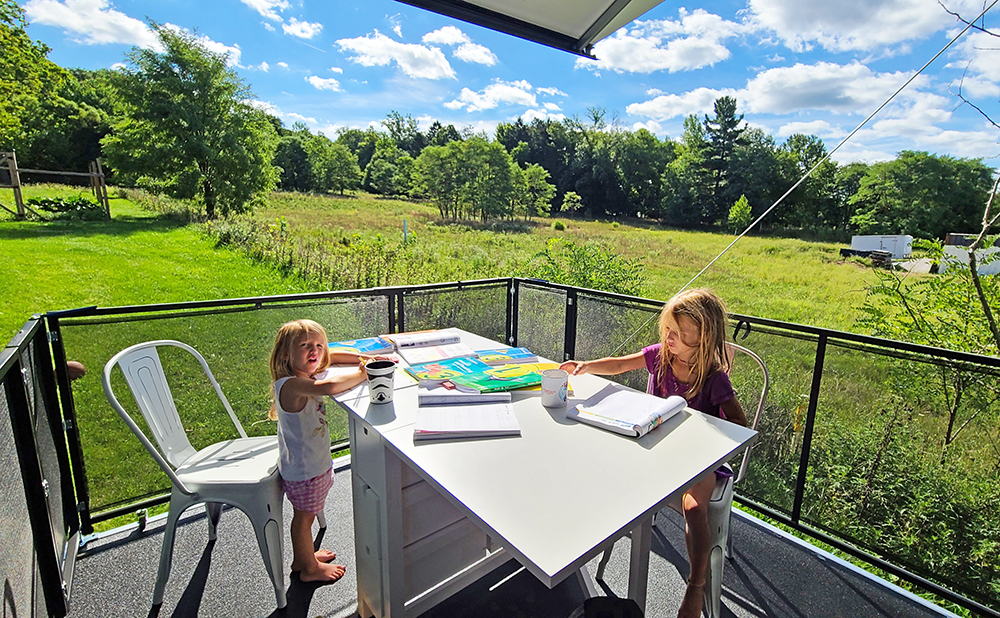 Two young girls on an RV toy hauler patio with a beautiful landscape behind them.