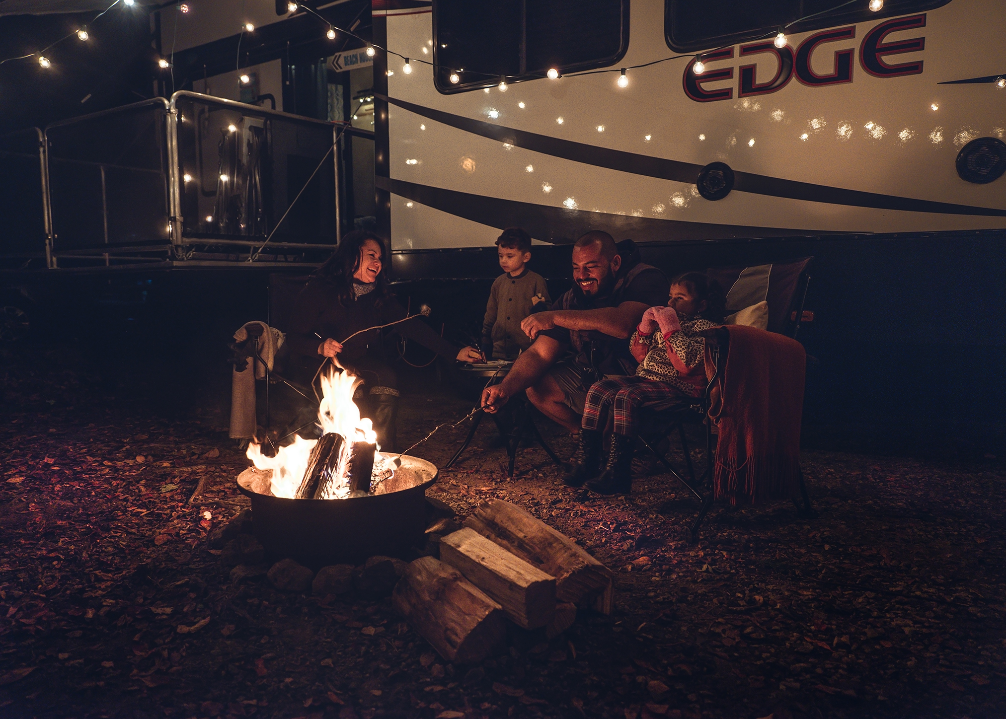 The Class family gathered around a campfire at night, with their toy hauler in the background.