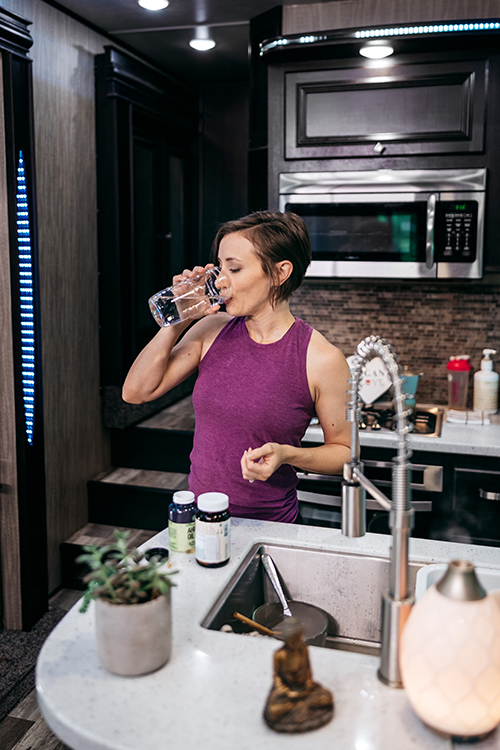 A woman drinking a glass of water and taking vitamins inside her RV kitchen.