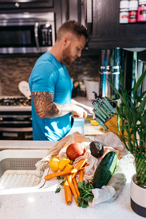 A man chopping up fruit in an RV kitchen with a bag of produce on the counter.