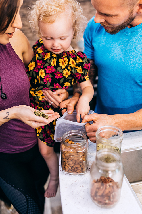 A woman, man and young child putting together a bag of trail mix with nuts and seeds.