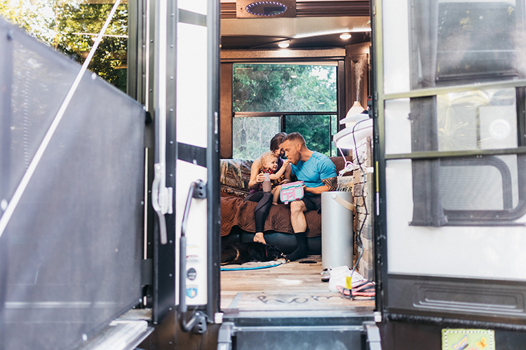 A man, woman and young child sitting together inside an RV, eating healthy snacks.