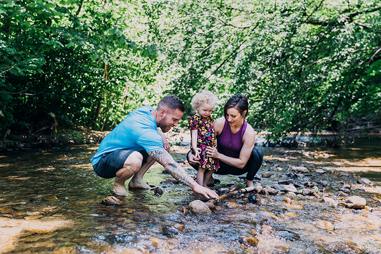 A man, a woman and a small child wading in a shallow stream together.