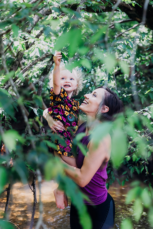 A woman holding a small child as they walk through nature.