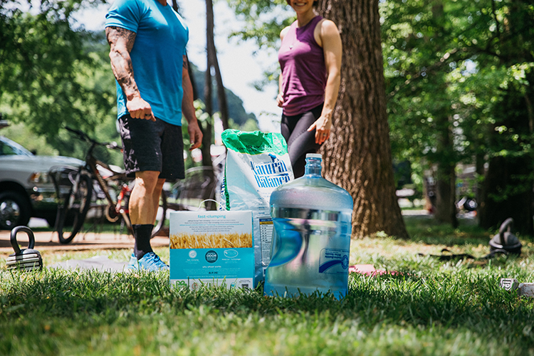 A man and a woman show off alternative items you can use for a resistance workout, including a five-gallon water jug, a box of cat litter and a big bag of dog food.
