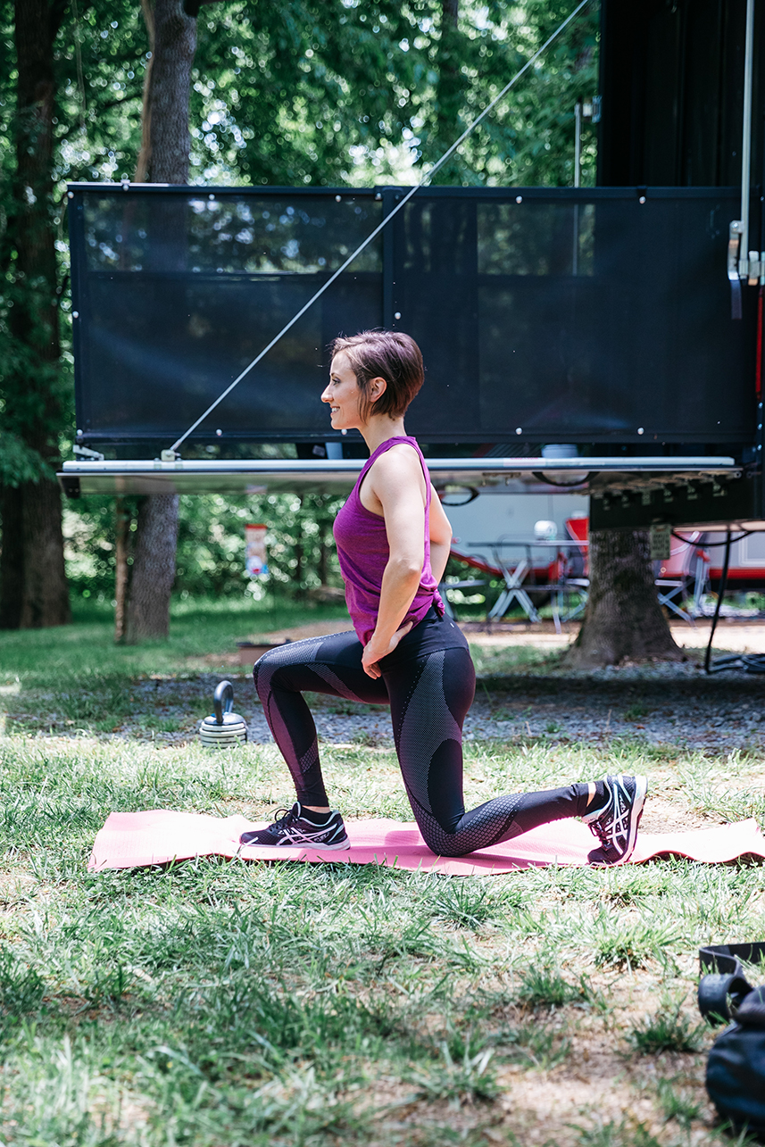 A fit woman does lunges on a yoga mat outside her RV at a camp site.