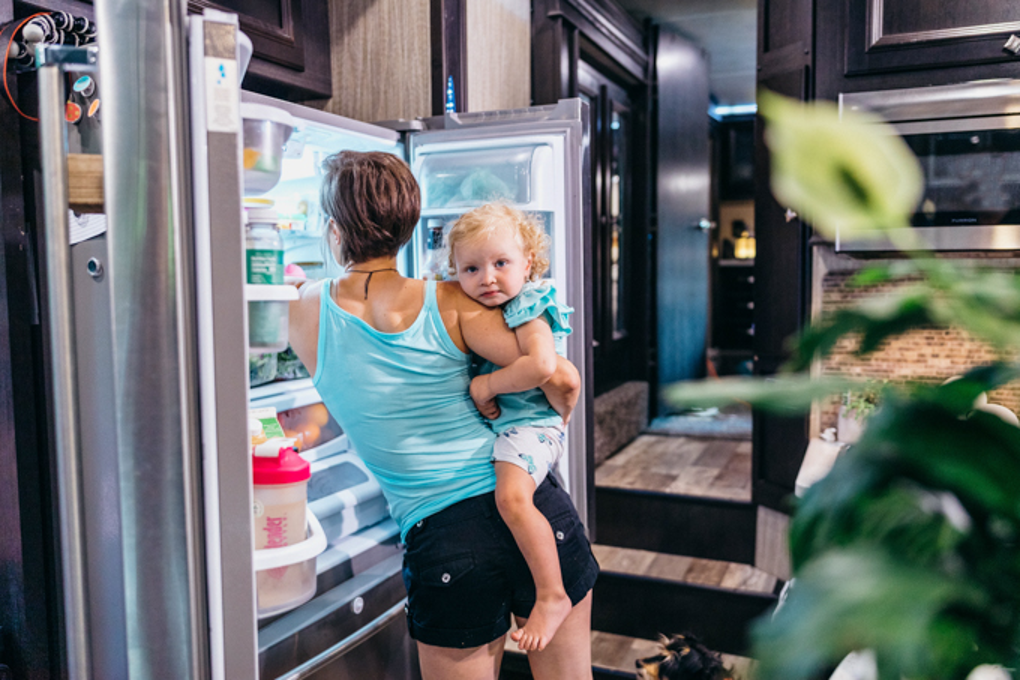A mom holding a small girl, reaching into a full-size fridge in an RV. 