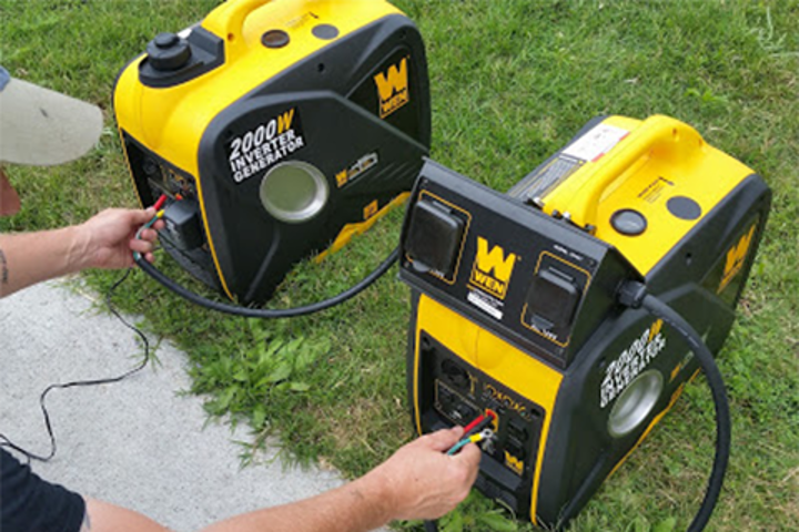 Two inverter generators sitting on the grass. 