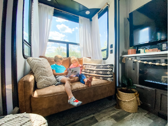 Two young kids looking at educational reading flashcards on a leather couch inside an RV.