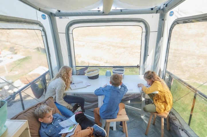 Four kids studying in an RV toy hauler with a tent covering.