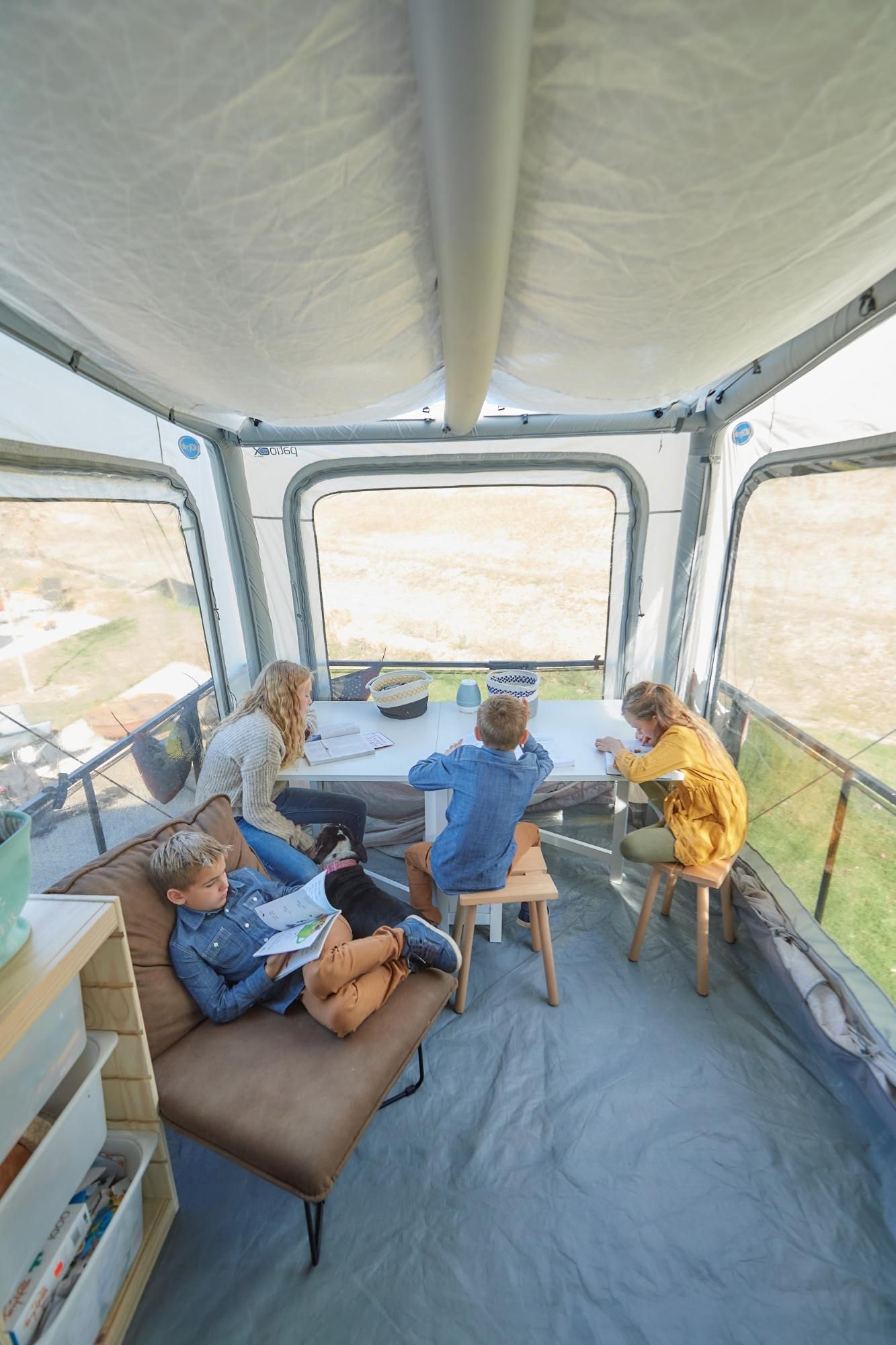 Four kids studying in an RV toy hauler with a tent covering.