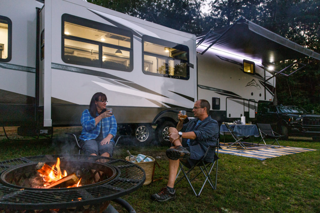 Two middle aged adults sitting near a fire outside an RV.