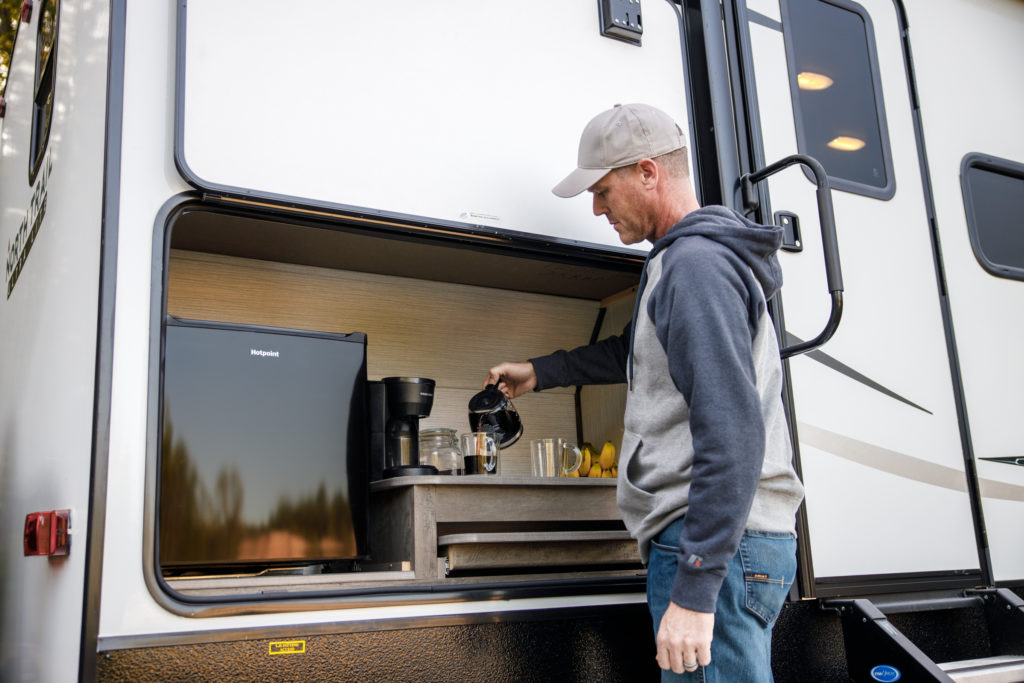 A man pouring coffee at an RV's outside kitchen.