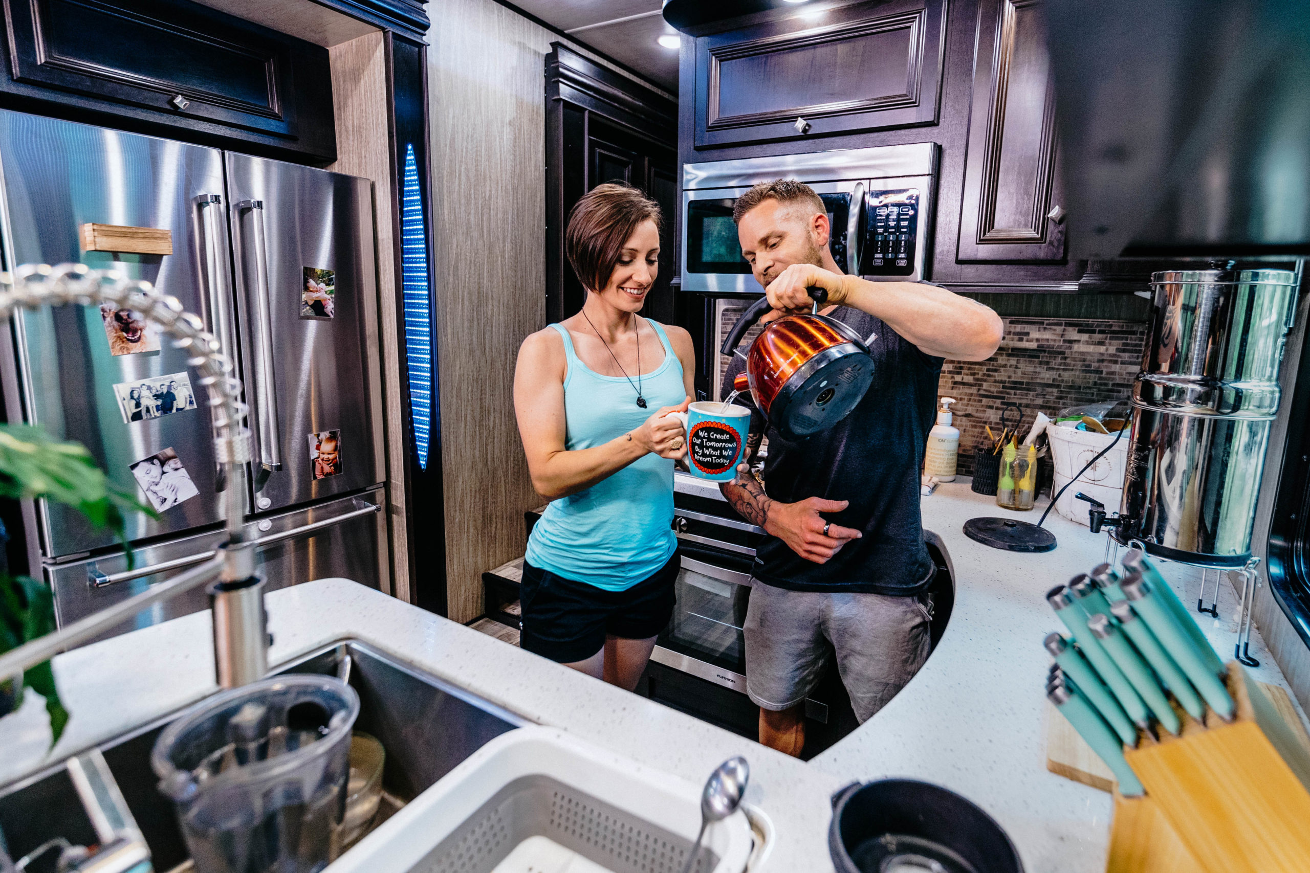 Two fit adults pouring coffee inside an RV kitchen.