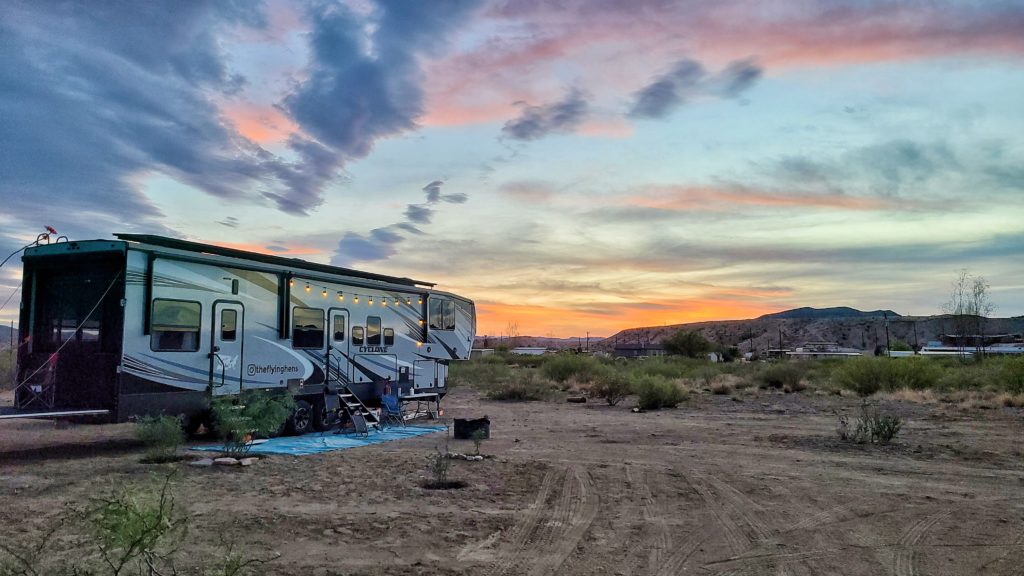 A Heartland RV boondocking in a desert landscape with the sun setting behind the hills.