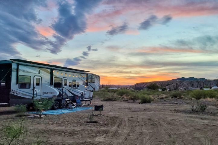 A Heartland RV boondocking in a desert landscape with the sun setting behind the hills.