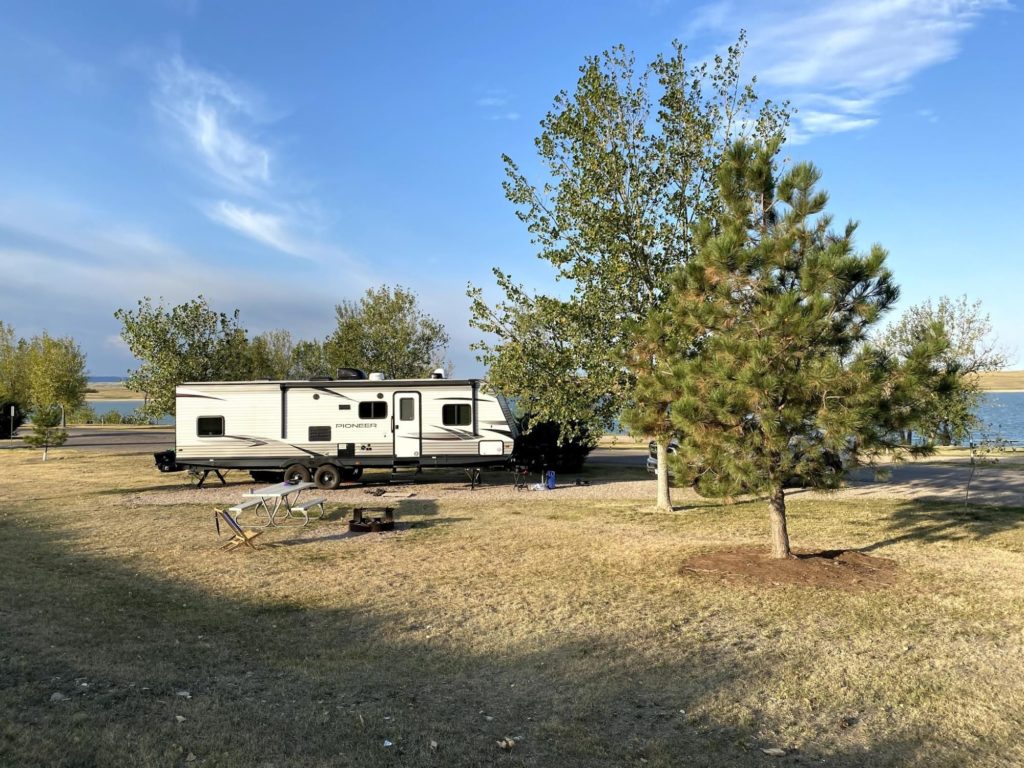 An RV parked in a sunny campsite with trees and water nearby.