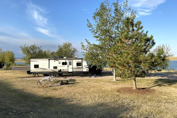 An RV parked in a sunny campsite with trees and water nearby.