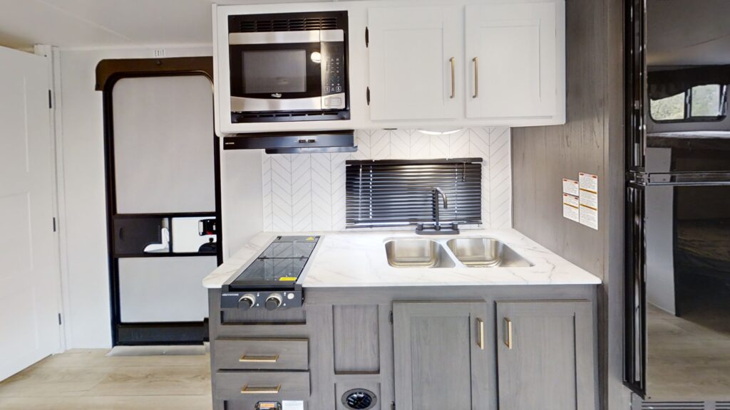 Modern kitchen in the Pioneer BH261 travel trailer, featuring stainless steel appliances, ample counter space, and wooden cabinetry with sleek finishes.