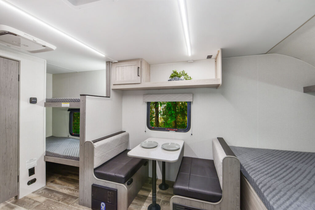 The image showcases the 2025 Mallard 17BHL travel trailer’s interior, designed for compact comfort and functionality. It features a cozy layout with a dinette area, well-equipped kitchen, and bunk beds, providing convenient sleeping and dining options. The design emphasizes practical use of space, with modern finishes and large windows that allow natural light to fill the space. Perfect for family outings or solo adventures, the 17BHL balances style and utility, making it an inviting choice for travelers seeking a cozy and efficient travel trailer.