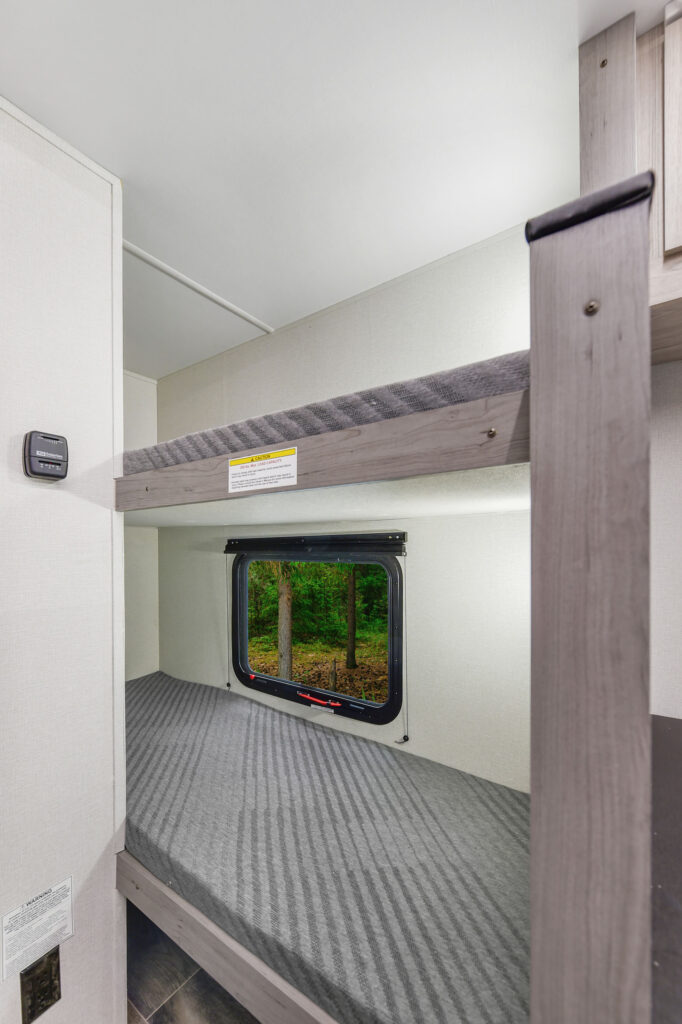 This image captures the well-equipped kitchen area of the 2025 Mallard 17BHL travel trailer, designed with convenience and style. The kitchen features a compact yet functional setup with a two-burner cooktop, microwave, and a sink, all integrated into a sleek countertop. Above, cabinets provide ample storage for kitchen essentials, while the modern backsplash adds a stylish touch. This kitchen is thoughtfully designed to maximize space, making meal prep easy and enjoyable, whether you’re at the campsite or on the road.