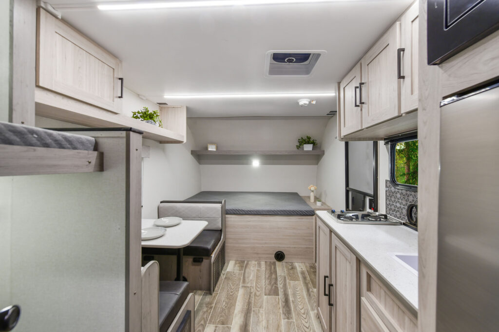 This image captures the cozy kitchen area of the 2025 Mallard 17BHL travel trailer, featuring compact yet functional appliances ideal for on-the-go meal prep. The kitchen includes a sleek countertop, a stove, and a refrigerator, all with a clean, modern finish. Ample cabinetry provides storage, while large windows above the workspace invite natural light, creating an airy, open feel. This kitchen setup is perfect for travelers who want a fully equipped, stylish cooking area within a compact layout.