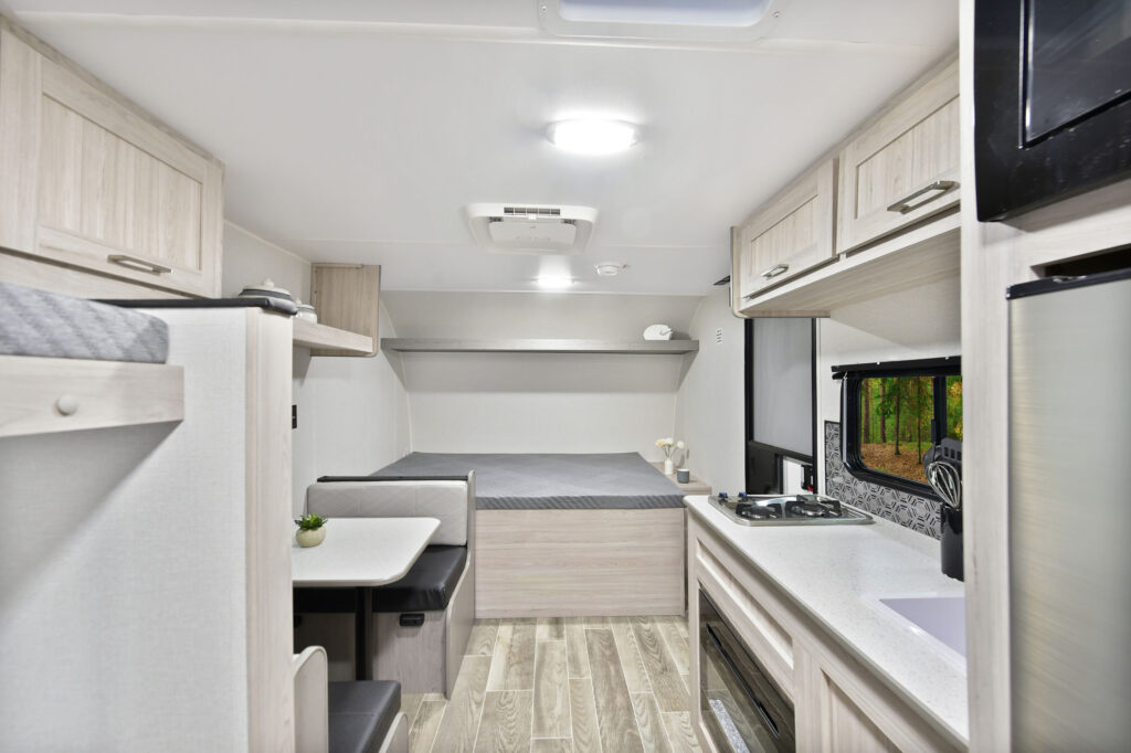 This image captures the cozy dinette area of the 2025 Prowler P17B travel trailer, featuring a comfortable booth-style setup with cushioned seats on both sides of a sturdy table. The space is framed by large windows, bringing in natural light and offering views of the outdoors, enhancing the dining or relaxation experience. With a mix of neutral and wood tones, the dinette blends functionality and warmth, perfect for meals, games, or relaxing in style while on the road.