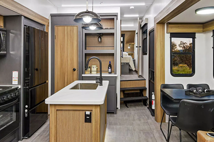 Inside a sleek 2025 RV, the kitchen and dining area offer panoramic windows framing a breathtaking sunset. Nearby, an inset reveals a group delighting in a lake boat ride, capturing the spirit of fifth wheels adventurous lifestyle.