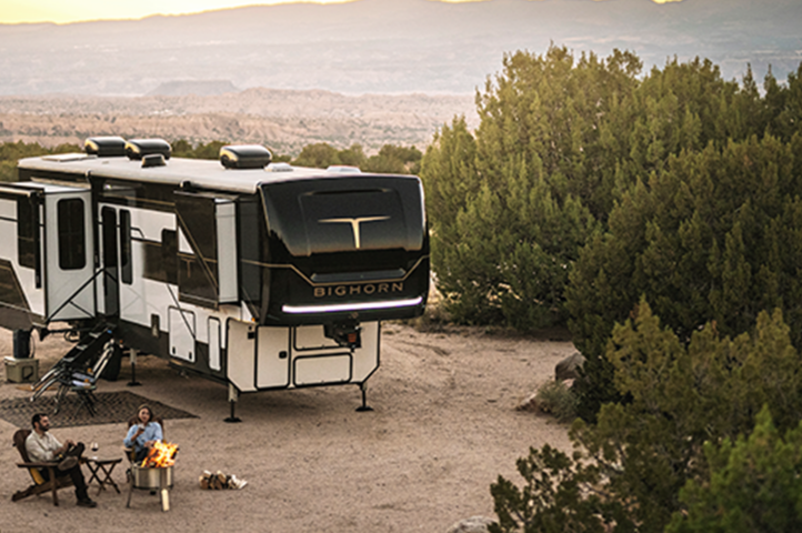 In a scenic desert area of 2025, a large RV is parked amid the trees. A family relaxes by a campfire, nestled into camping chairs with a table nearby. The sun sets in the distance, casting its warm glow over this serene landscape.