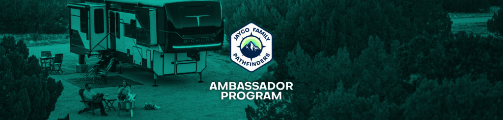 A large RV is parked at a campsite surrounded by trees. Two people sit in chairs by a campfire. The image features a Jayco Remote Pathfinders badge and the text Ambassador Program in bold letters.